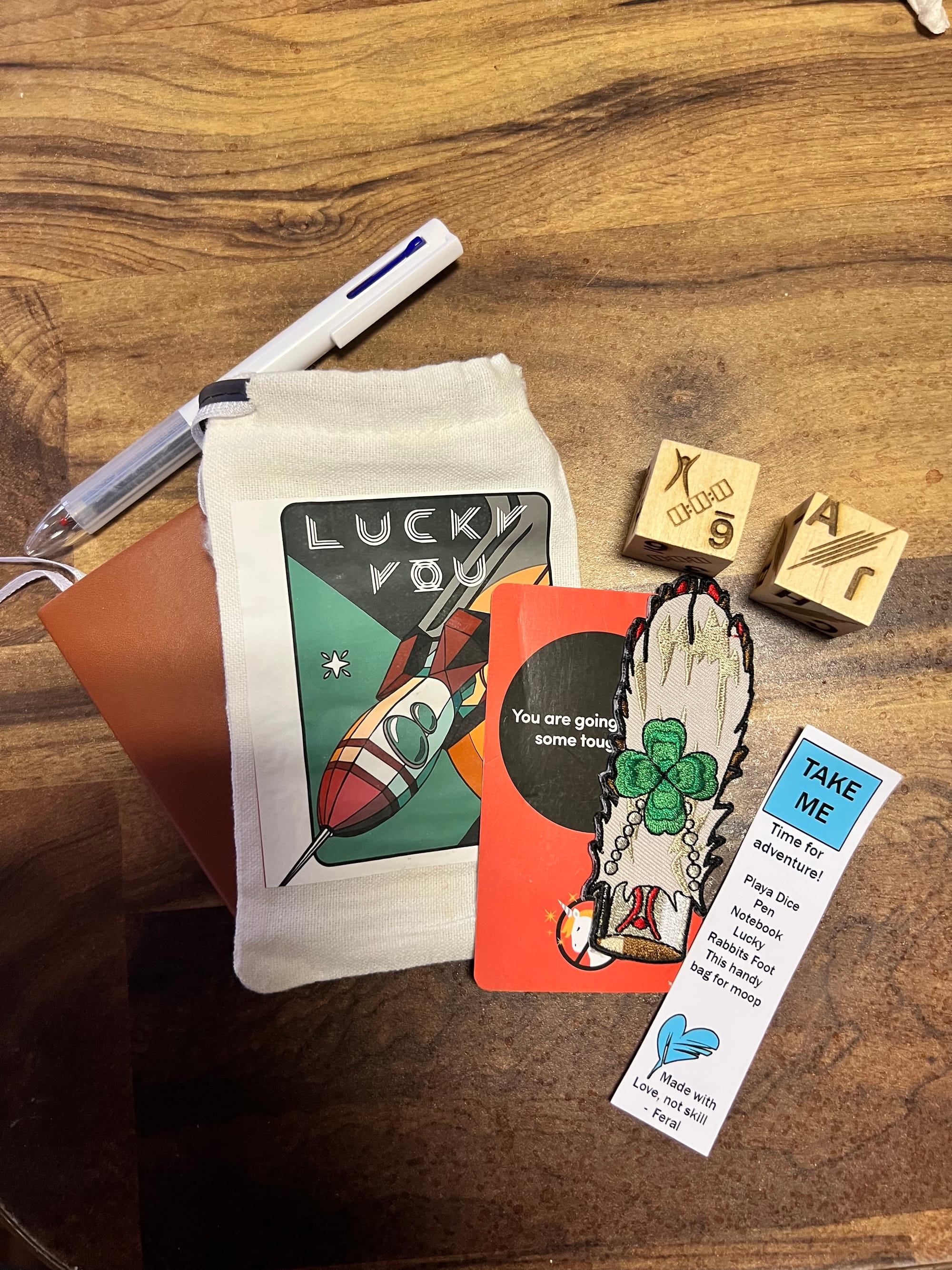 A small “Lucky You” bag found in deep playa, containing a rabbit’s foot patch, carved wooden burner dice, a notebook, and a pen — one of twenty hidden gifts.