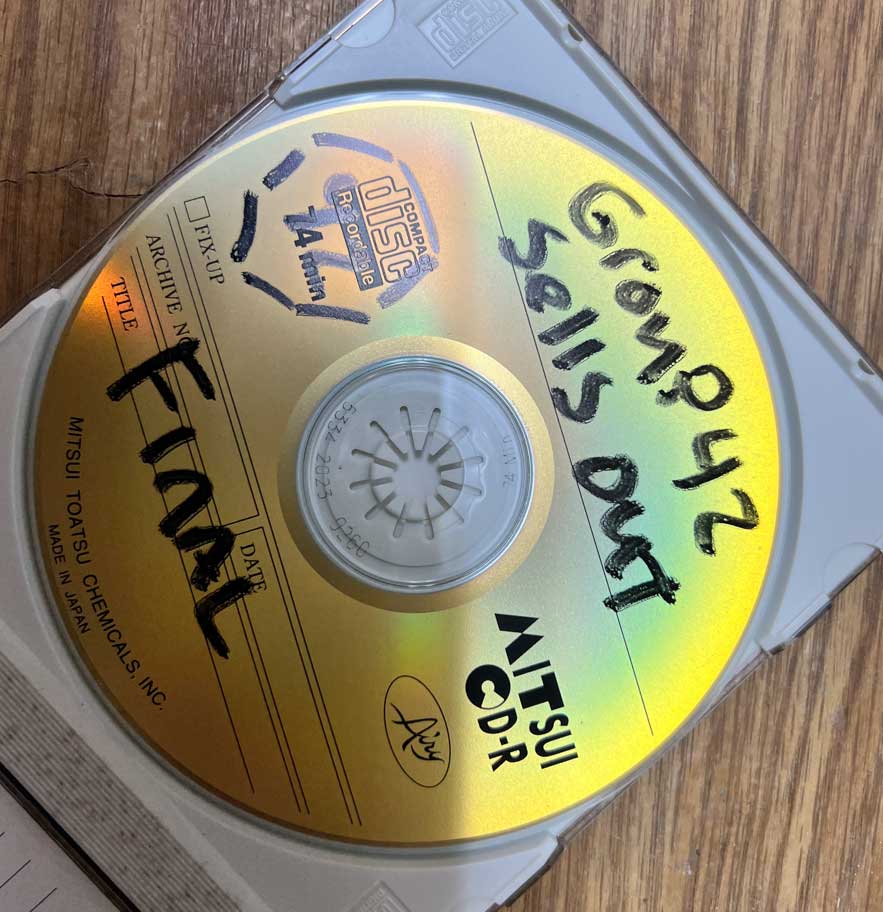 CD-R in a jewel case, hand-labeled “Group42 Sells Out – Final,” resting on a wooden surface.